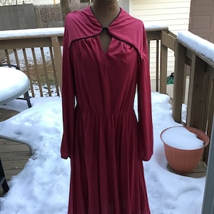 May include: A long-sleeved, crimson red dress with a V-neckline and a black trim around the neckline. The dress has a gathered waist and a flowing skirt.