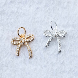 May include: Two small bow charms, one gold and one silver, with clear crystal embellishments.