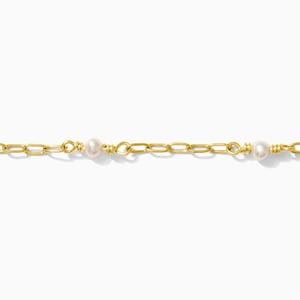 Puede incluir: Delicado collar de cadena dorada con tres pequeñas perlas blancas espaciadas. La cadena tiene un diseño de eslabones y está sobre un fondo blanco.