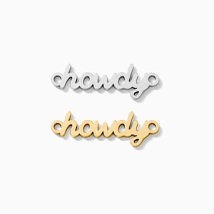 May include: Two metal pendants in a cursive font that spell out the word "howdy". One pendant is silver, and the other is gold. Both pendants have small loops on each end for attaching to a chain or other jewelry.