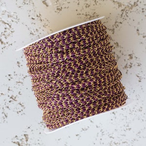 May include: A spool of gold and purple chain. The chain is wound around a white spool.