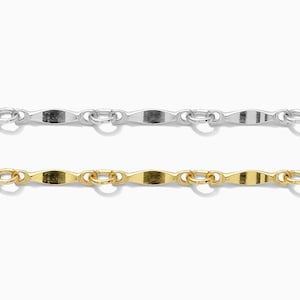 Puede incluir: Dos delicados collares, uno plateado y otro dorado, se muestran sobre un fondo blanco. Las cadenas presentan un patrón repetitivo de pequeños eslabones alargados conectados por anillos circulares, creando un aspecto refinado y elegante. Joyería.