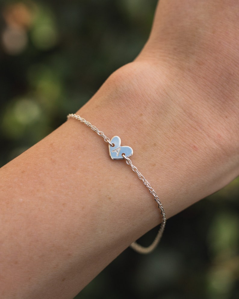 May include: A silver chain bracelet with a heart-shaped charm engraved with the letter "A".