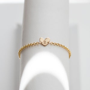 May include: A gold chain bracelet with a heart-shaped charm featuring the letter "B" engraved on it.