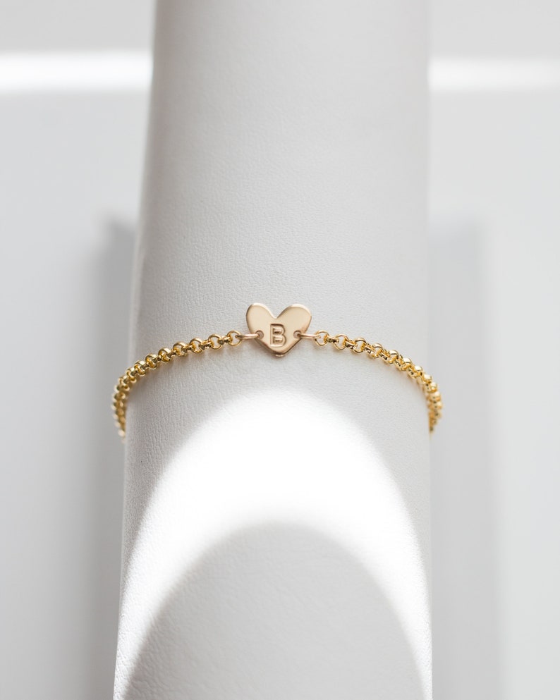 May include: A gold chain bracelet with a heart-shaped charm featuring the letter "B" engraved on it.