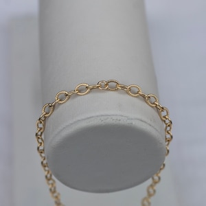 Op de afbeelding: Een gouden kettingarmband met een delicaat, ovaalvormig schakeld ontwerp.