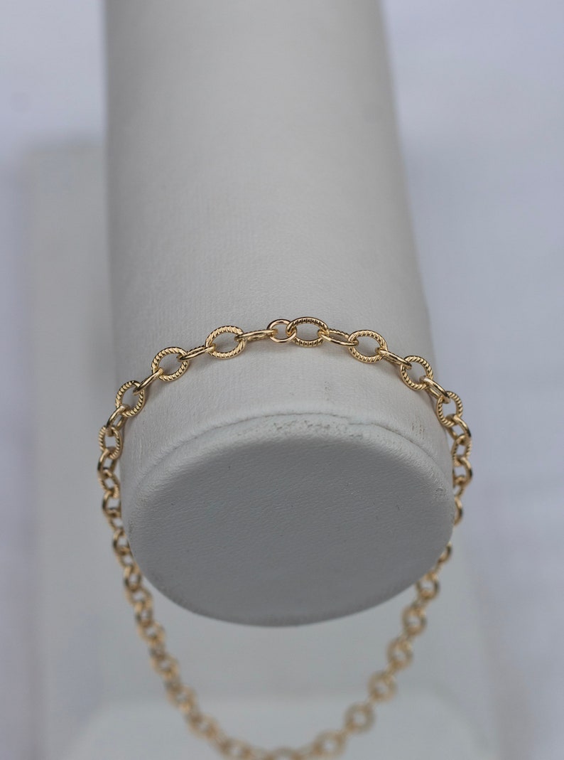 Op de afbeelding: Een gouden kettingarmband met een delicaat, ovaalvormig schakeld ontwerp.