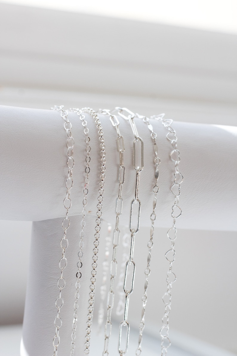 May include: A collection of six silver chains of different styles and lengths, displayed on a white surface.