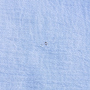 May include: Two small hoop earrings, one silver and one gold, on a light blue fabric background.