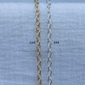 Op de afbeelding: Twee kettingen, een gouden en een zilveren, worden getoond tegen een witte achtergrond. De gouden ketting is gemarkeerd met "G44" en de zilveren ketting met "S44".