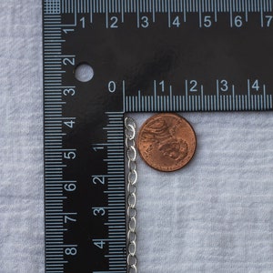 Op de afbeelding: Een zilveren kettingketting naast een Amerikaanse penny. De ketting is ongeveer 45 cm lang en heeft een delicaat ontwerp.