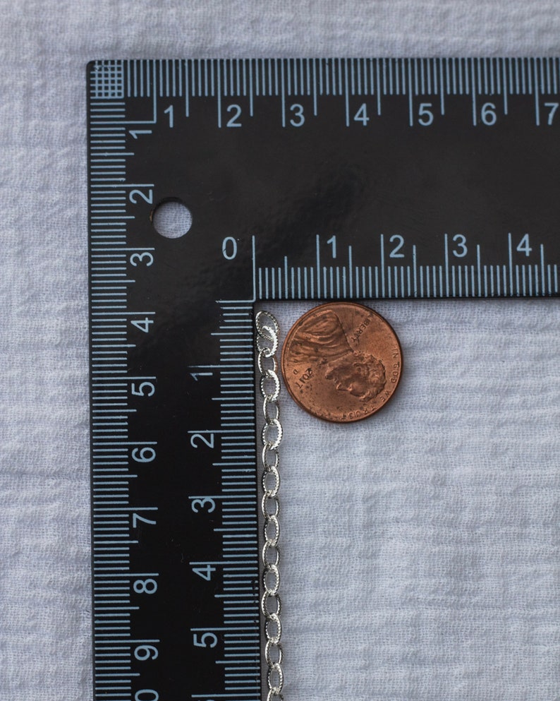 Op de afbeelding: Een zilveren kettingketting naast een Amerikaanse penny. De ketting is ongeveer 45 cm lang en heeft een delicaat ontwerp.