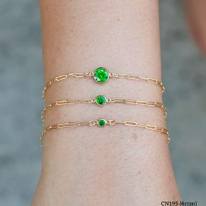 May include: Three gold chain bracelets with green gemstone accents. The bracelets are layered on a person's wrist. The gemstones are different sizes: 6mm, 4mm, and 3mm.