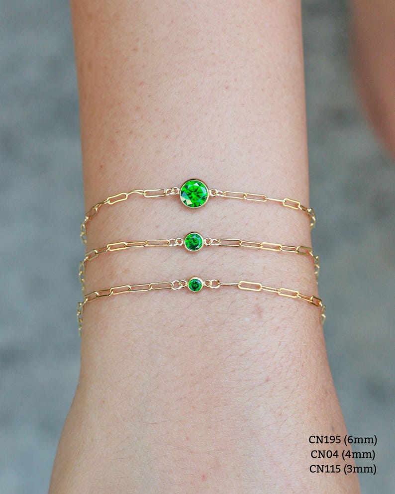 May include: Three gold chain bracelets with green gemstone accents. The bracelets are layered on a person's wrist. The gemstones are different sizes: 6mm, 4mm, and 3mm.
