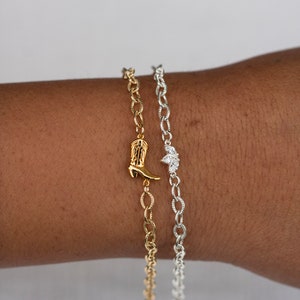 Op de afbeelding: Twee gouden kettingarmbanden met bedels. De ene armband heeft een kleine laarsbedel, de andere heeft een bedel met drie kleine diamanten.