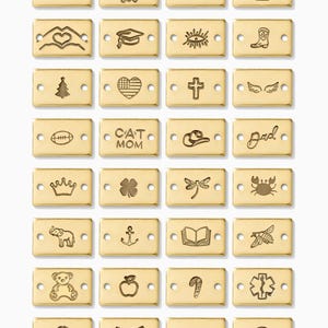 May include: A collection of gold-colored rectangular charms with various engraved designs, including a graduation cap, heart, cross, wings, and a football. Other charms feature the words "CAT MOM" and "dad".