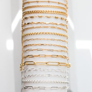May include: A display of gold and silver chains of various styles and sizes. The chains are arranged vertically on a white background.