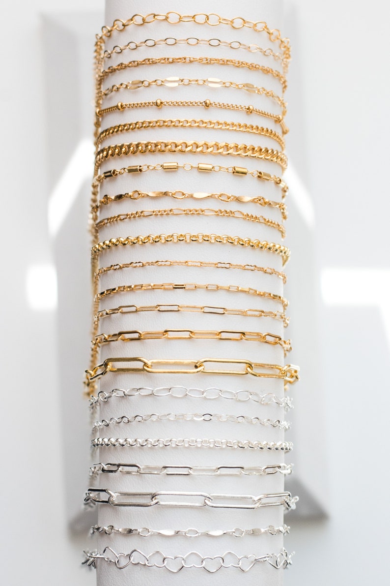 May include: A display of gold and silver chains of various styles and sizes. The chains are arranged vertically on a white background.