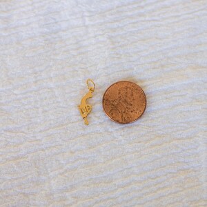 Pode incluir: Um amuleto dourado em forma de pistola, ao lado de um centavo americano.