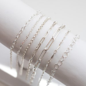 May include: A set of six silver chain bracelets with different link styles, displayed on a white surface.