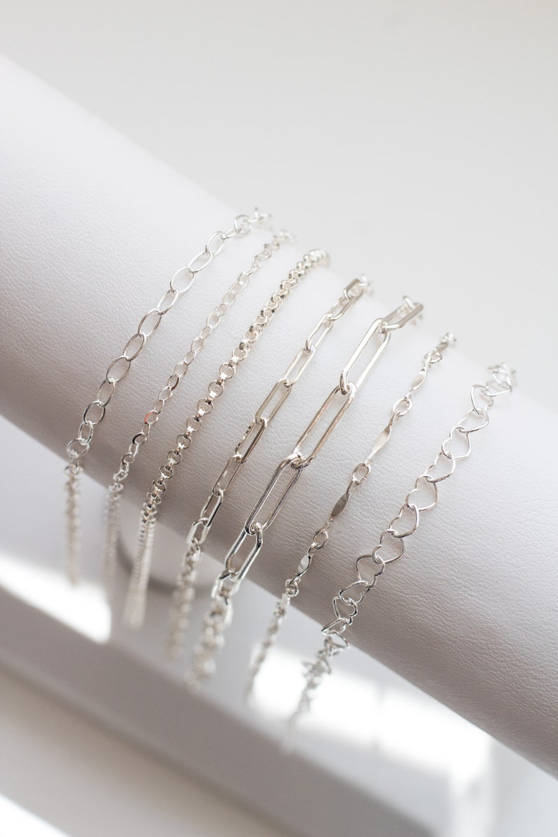 May include: A set of six silver chain bracelets with different link styles, displayed on a white surface.