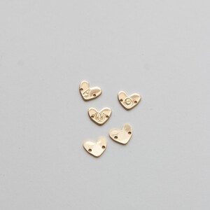 May include: Five gold heart-shaped charms with the letters A, W, and O engraved on them. The charms have two holes on each side.