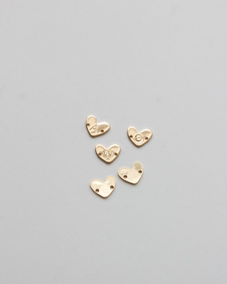 May include: Five gold heart-shaped charms with the letters A, W, and O engraved on them. The charms have two holes on each side.