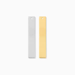 May include: Two rectangular metal pendants, one silver and one gold, are displayed against a white background. Each pendant has a small hole at the top for attaching to a chain or cord. The pendants are simple and modern.