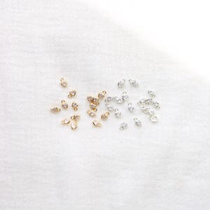 Puede incluir: Una colecci&oacute;n de peque&ntilde;os dijes en forma de coraz&oacute;n. Algunos son dorados con piedras transparentes, mientras que otros son plateados con piedras transparentes. Los dijes est&aacute;n dispersos sobre una superficie blanca y texturizada.