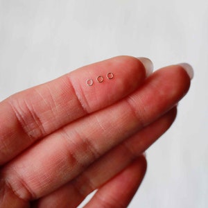 May include: Four small, gold-colored hoop earrings, displayed on a finger.
