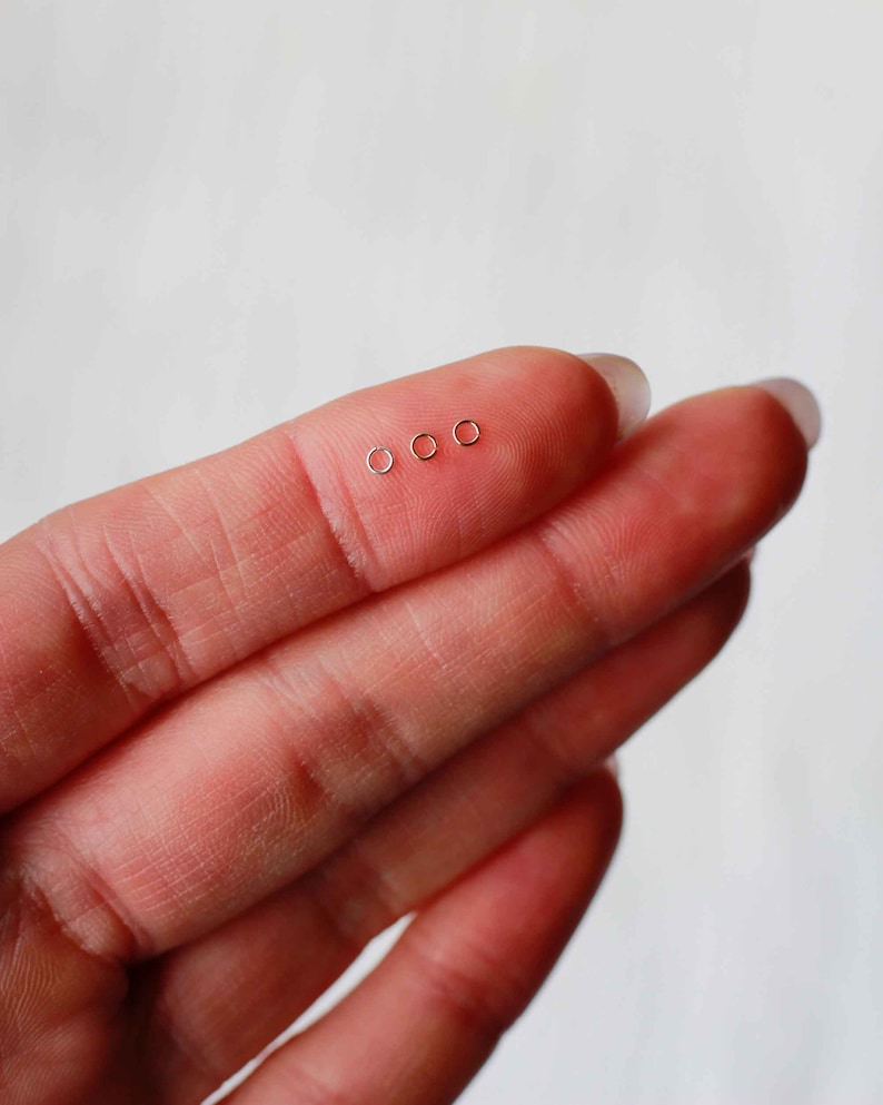 May include: Four small, gold-colored hoop earrings, displayed on a finger.