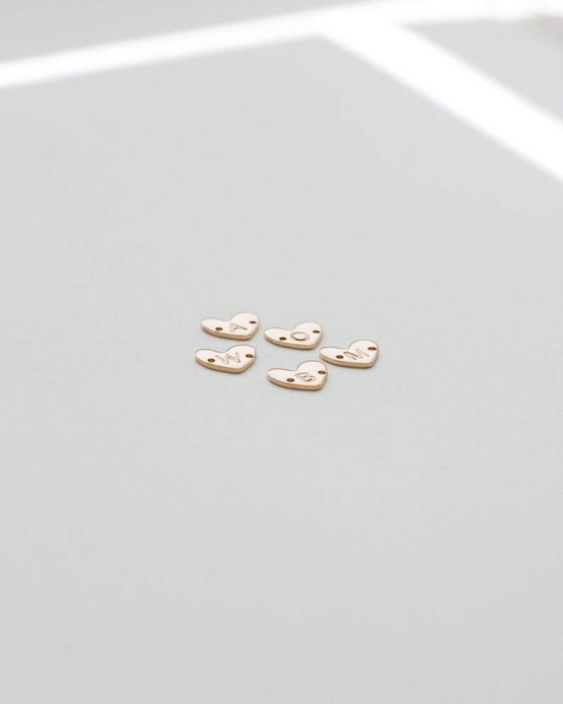 May include: Five gold heart-shaped charms with the letters W, O, M, A, and N engraved on them.