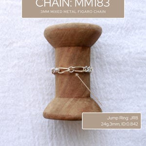 May include: A silver and gold mixed metal Figaro chain, 3mm wide, is shown on a wooden spool. The image also shows a jump ring with the text "Jump Ring: JR8 24g.3mm, ID:0.842" and the text "CHAIN: MM183 3MM MIXED METAL FIGARO CHAIN". The chain is a jewellery item.