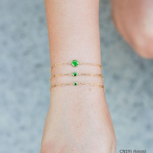 May include: Three gold chain bracelets with green gemstones. The bracelets are layered on a person's wrist. The gemstones are different sizes: 6mm, 4mm, and 3mm.
