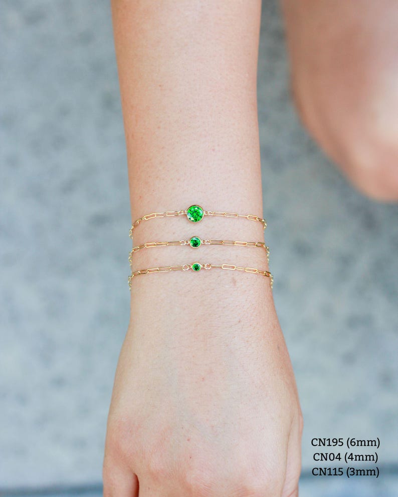 May include: Three gold chain bracelets with green gemstones. The bracelets are layered on a person's wrist. The gemstones are different sizes: 6mm, 4mm, and 3mm.