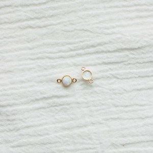 Puede incluir: Dos peque&ntilde;os conectores de joyer&iacute;a dorados, cada uno con una piedra redonda iridiscente similar al &oacute;palo. Los conectores tienen peque&ntilde;os bucles a cada lado para sujetarlos a otros componentes de joyer&iacute;a. El fondo es una tela blanca texturizada.