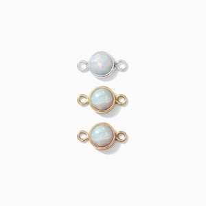 May include: Three opal connectors in silver, gold, and rose gold. Each connector features a round opal stone with a pearlescent sheen, set within a delicate metal frame with small loops on either side for attachment. The connectors are displayed against a white background.