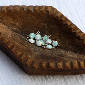 Puede incluir: Un conjunto de peque&ntilde;os colgantes de &oacute;palo ovalados con engastes plateados. Los &oacute;palos tienen una base blanca lechosa con destellos iridiscentes azules y verdes. Los colgantes est&aacute;n dispersos sobre una superficie de madera oscura.