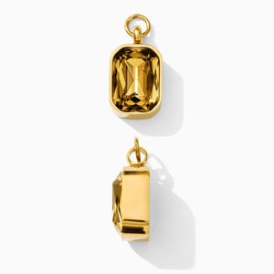 May include: Two rectangular pendants featuring faceted amber-colored crystals set in polished gold-tone metal frames. Each pendant includes a small circular jump ring at the top for attachment, shown from both a front-facing and a side-profile view.