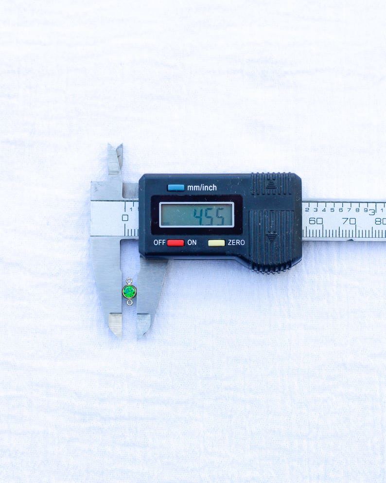 May include: A digital caliper measuring a small green gemstone pendant. The caliper reads 4.55 mm.