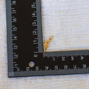 Pode incluir: Um amuleto dourado em forma de pistola com as letras "11" gravadas no lado. O amuleto &eacute; medido com uma r&eacute;gua.