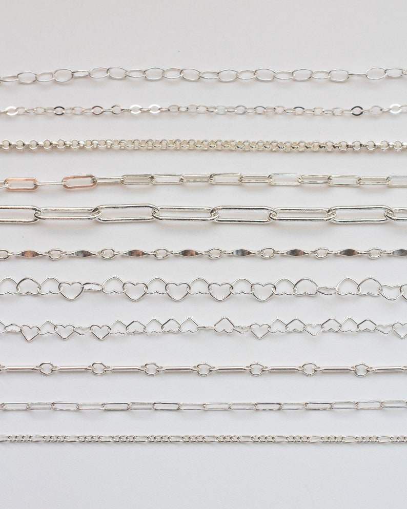 May include: A collection of ten silver chains of different styles and sizes, laid out horizontally on a white background.