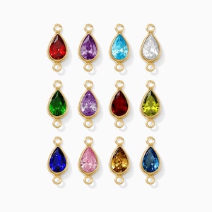 May include: A collection of twelve teardrop-shaped pendants with various colored gemstones. Each gem is set in a gold-colored bezel and features a small loop at the top and bottom for attachment. The gemstones include red, purple, blue, white, green, and yellow.