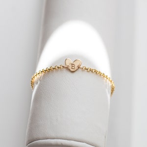 May include: A gold chain bracelet with a small heart charm featuring the letter "B" engraved on it.