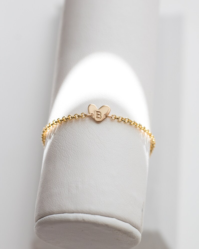 May include: A gold chain bracelet with a small heart charm featuring the letter "B" engraved on it.
