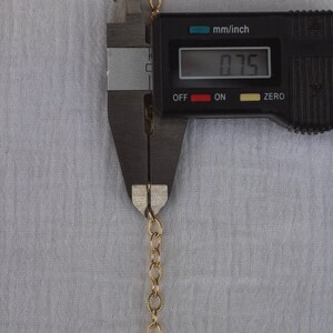 Op de afbeelding: Een gouden ketting wordt gemeten met een digitale schuifmaat. De schuifmaat geeft 0,75 mm/inch aan.