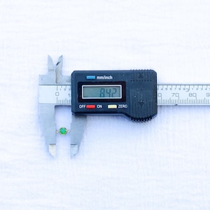 May include: A close-up of a digital caliper measuring a small green gemstone. The caliper reads 8.42 mm.