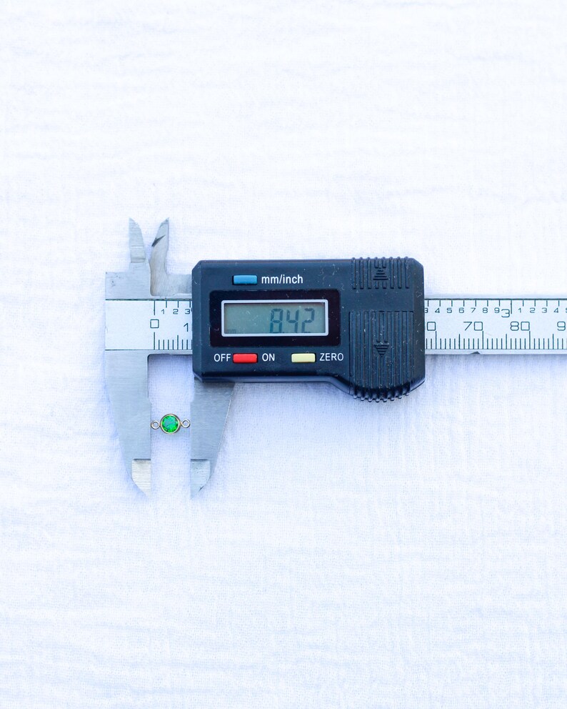 May include: A close-up of a digital caliper measuring a small green gemstone. The caliper reads 8.42 mm.