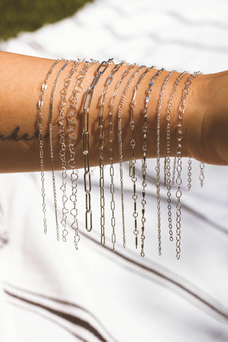 May include: A collection of silver chain bracelets with different link styles, including heart, oval, and square links.