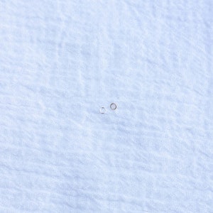 May include: Two small hoop earrings, one silver and one gold, on a white fabric background.